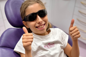 an image of a child sitting in the dental chair wearing protective dental glasses with her thumbs up, showing calm and confidence in the dental practice london
