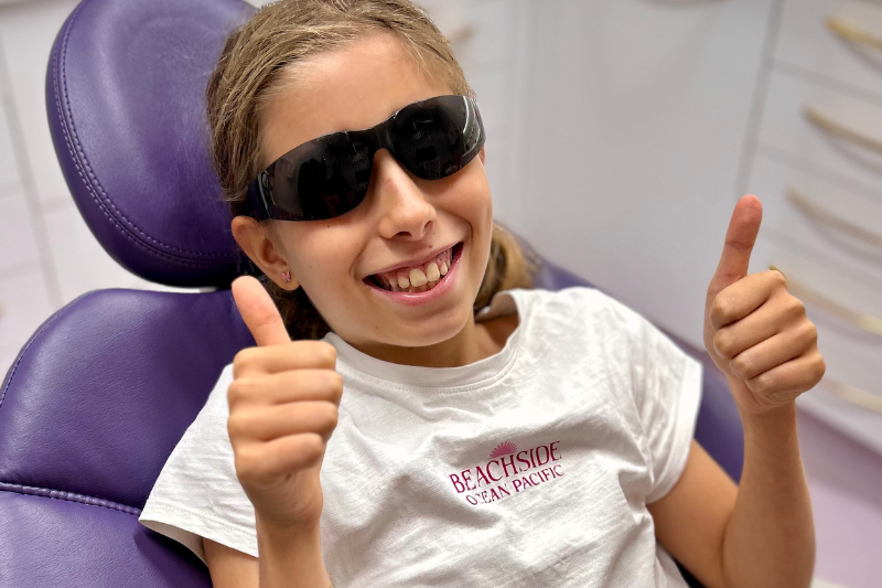 an image of a child sitting in the dental chair wearing protective dental glasses with her thumbs up, showing calm and confidence in the dental practice london
