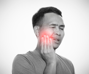 a black and white image of a man holding a painful part of his ace, with red glowing detail to emphasise tooth and dental pain in london