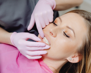 an image of a woman wearing a pink tshirt laying in a dental chair having her gums examined by a dentist wearing white gloves
